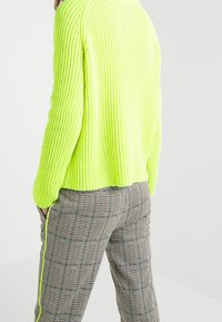 Neonowo zielony prążkowany sweter o luźnym kroju, zestawiony z kratkowymi spodniami w czarno-białą kratę z zielonymi akcentami, z bocznym paskiem.