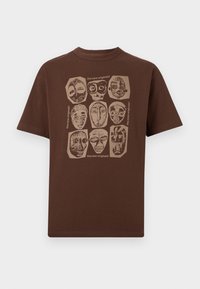 Braunes T-Shirt mit kurzen Ärmeln und beigen Stammesmasken-Designs in einem 3x3-Raster sowie dem Text "the new originals" um die Masken auf der Brust.