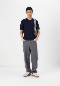 Polo tricotat bleumarin cu guler în V și dungi, asortat cu pantaloni largi din bumbac gri și adidași albi cu accente negre.