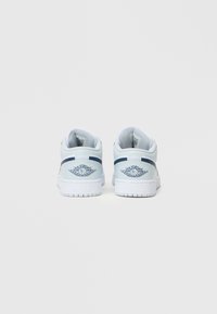 Niskie trampki w jasnoniebieskiej i białej skórze, z granatowym paskiem i skrzydlatym logo na pięcie, teksturowana powierzchnia i biała podeszwa.