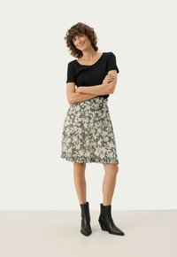 Sort tekstureret kortærmet top kombineret med en let, blomstermønstret nederdel i creme og grå. Modellen har sorte ankelstøvler på.