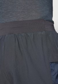 Herrarnas sportshorts i mörkgrått tyg, elastisk midja, sidoficka och strukturerad panel på ena sidan för ökad andningsförmåga.