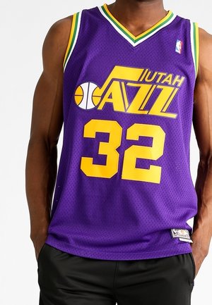 Man draagt een paarse Utah Jazz basketbaljersey met gele nummer 32 en groen, wit en geel afwerking aan de halslijn en mouwen.