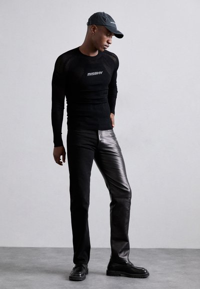 Haut à manches longues en maille noire avec logo, associé à un pantalon en cuir noir brillant et des chaussures noires, complété par une casquette noire.
