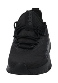 Svart idrottssko med ovandel i nät, rund tå och platta snören. Har en logotyp på tungan och en strukturerad gummisula.