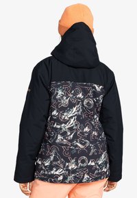 Schwarze Jacke mit einem gemusterten Rücken, der Berge und Text in Koralle und Blaugrün zeigt. Enthält eine Kapuze und wird mit einer rosa Mütze kombiniert.
