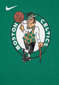 Grafika Boston Celtics prikazuje kartonskega leprechauna v zeleni brezrokavnik s shamrocki, ki drži košarko in palico, postavljen na zeleni majici.