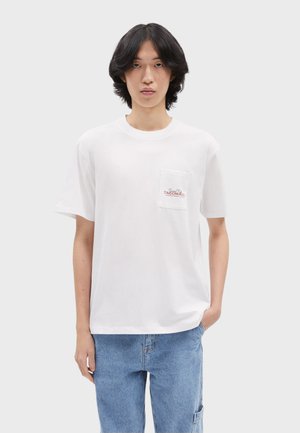 White short-sleeve t-shirt made of cotton, featuring a chest pocket with red logo text. Relaxed fit, smooth texture, and rounded neckline.