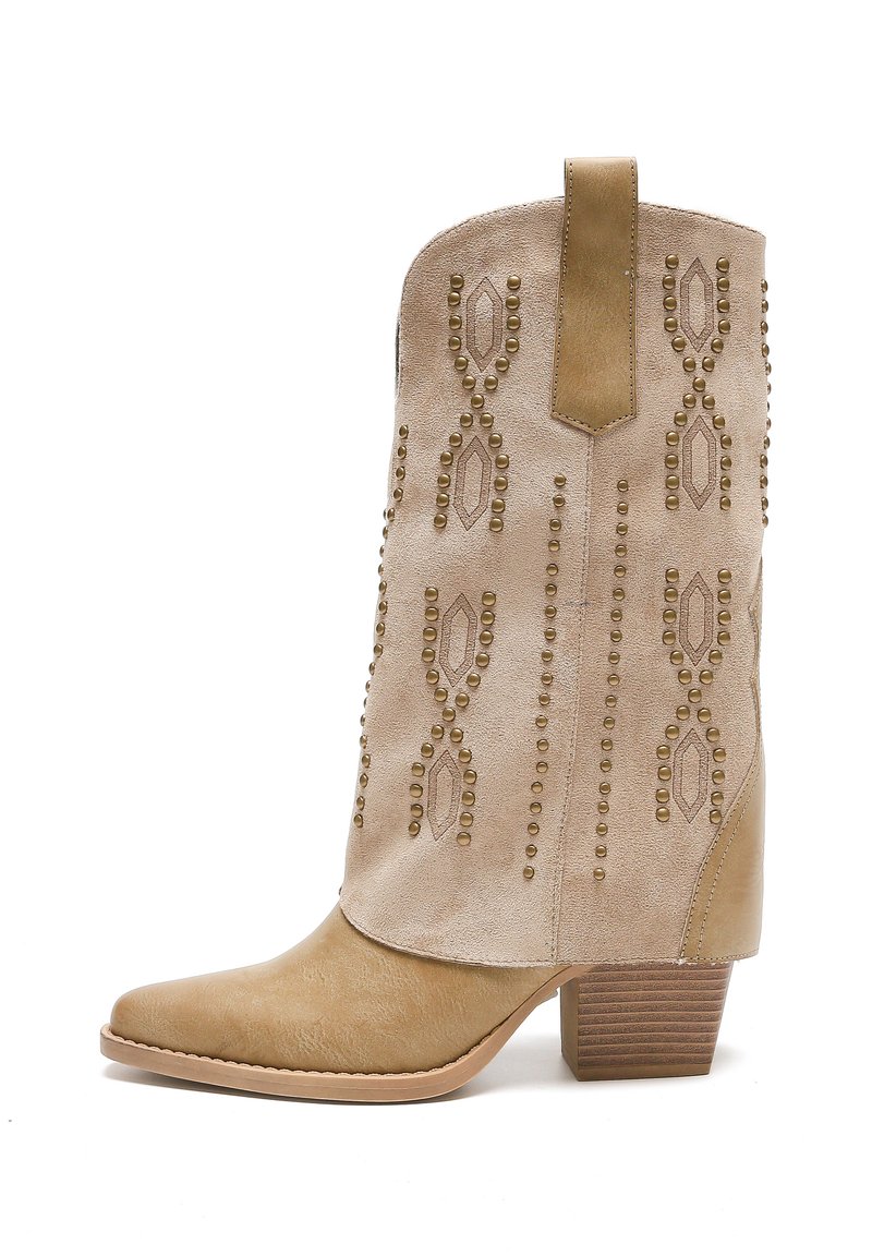 Botín de tobillo de ante beige con punta afilada, patrón decorativo de tachuelas y tacón de madera apilada. Presenta un tirador para facilitar su uso.