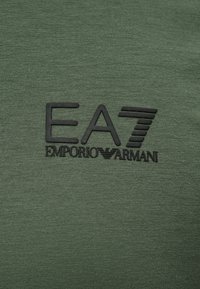 Πράσινο ύφασμα με ανάγλυφο μαύρο λογότυπο EA7 Emporio Armani στο κέντρο.