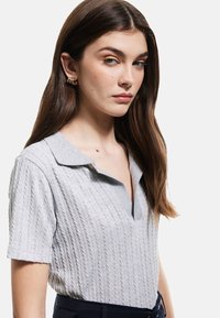 Grå kortærmet polo med struktureret ribbet design og krave, der har en knaplås og et diskret V-formet snit.
