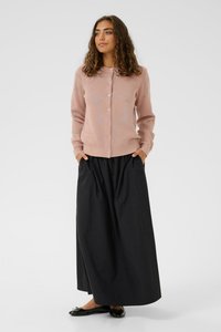 Helle rosa Strickjacke mit einem dezenten Muster und passenden Knöpfen, kombiniert mit einem langen schwarzen Rock und schwarzen Ballerinas.