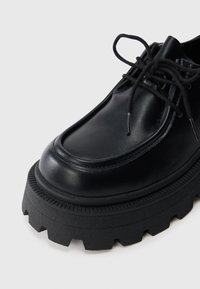 Must maagaga mustad nahast kingad ümara varbaga, millel on paks, sakiline must tald ja mustad paelad. Sile tekstuur koos peente tikandite detailidega.