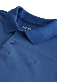Camisa polo azul hecha de tejido texturizado, presenta una tapeta de dos botones, logo bordado en el pecho y un suave cuello doblado.
