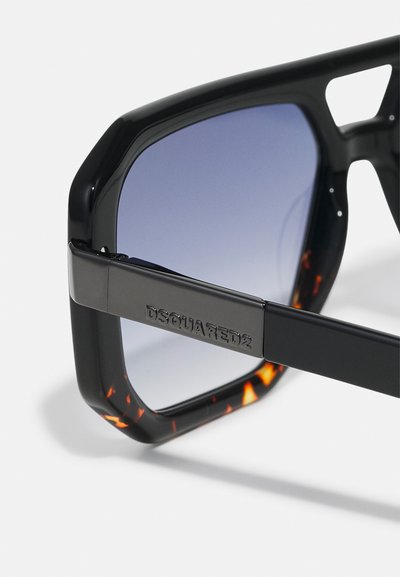 Ochelari de soare negri cu un design geometric, lentile gradiente albastre și un model de broască țestoasă pe brațul interior. Logo gravat pe tâmplă.