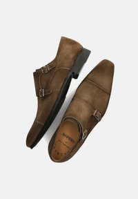 Braune Wildleder-Monks mit spitzer Kappe, doppelten Schnallen und schwarzer Laufsohle, mit glatter, weicher Textur.