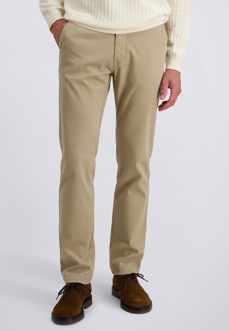 Chino beige en coton, avec une coupe droite et des poches latérales. Portés avec des chaussures en daim marron.