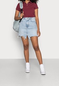 Džínová sukně s roztrhaným lemem, světle modrá barva, spárovaná s burgundským polo tričkem a bílými vysokými teniskami. Černý batoh na rameni.