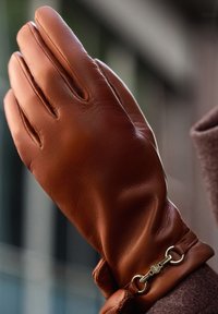 Brown leather glove with seam details, featuring a gold-tone hardware accent at the wrist for adjustment. Smooth texture, fitted design.