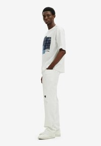 Camiseta de algodón blanca con un gráfico estampado azul en el frente, combinada con jeans blancos desgastados y zapatillas blancas.