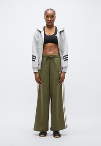 Γκρι φούτερ με φερμουάρ και μαύρες ρίγες, μαύρο αθλητικό μπουστάκι και χακί φαρδιά αθλητική φόρμα με λευκές πλευρικές ρίγες, συνδυασμένα με μαύρα παπούτσια.