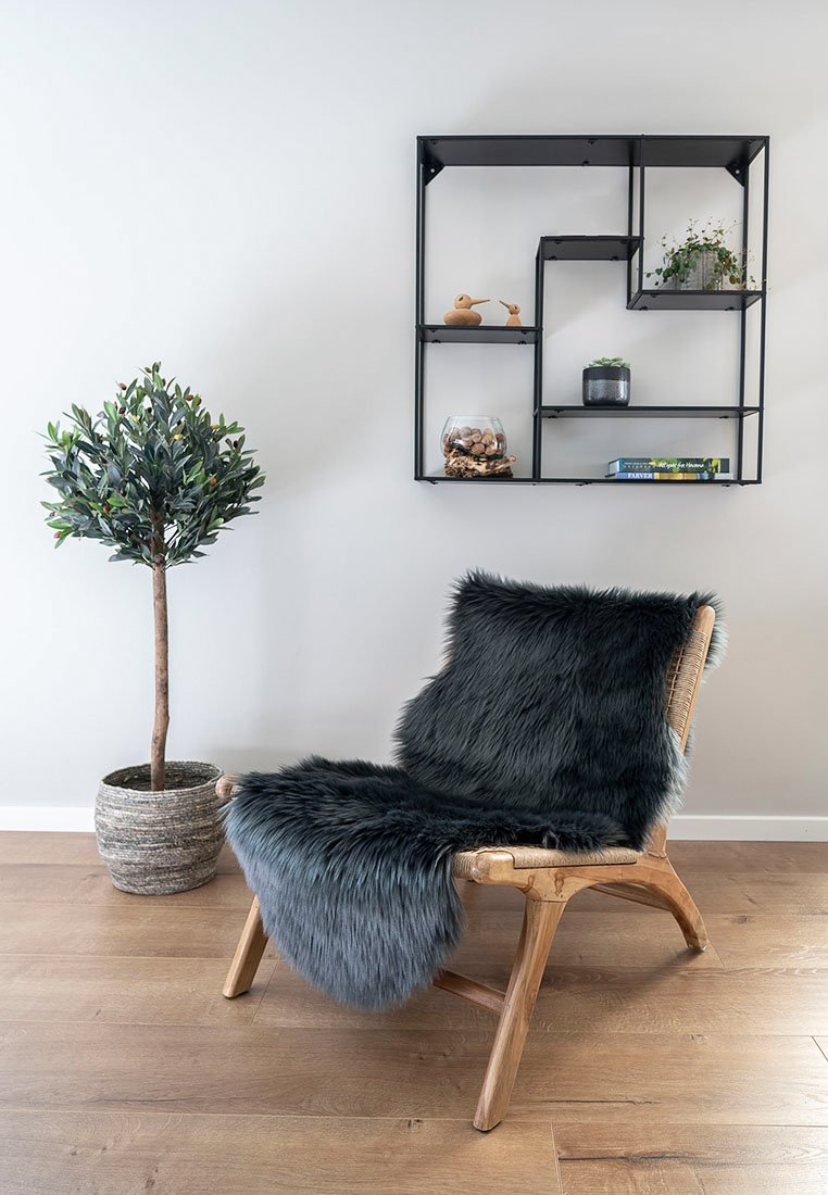 Holzstuhl mit grauem Kunstfell-Sitzbezug; verfügt über Beine aus Naturholz und eine strukturierte Oberfläche. Dekoriert mit einer Topfpflanze und einem geometrischen Regal.