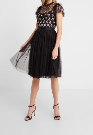 Robe en tulle noir avec broderie florale, corsage en maille transparente, manches à volants, taille cintrée et jupe évasée, associée à des sandales à lanières.