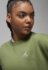 Felpa verde con tessuto a trama; presenta un logo Jordan ricamato bianco sul petto e un colletto a girocollo.