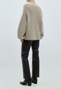 Beiger, grobmaschiger Strickpullover mit lockerer Passform und weiten Ärmeln, kombiniert mit schwarzen, synthetischen Lederhosen. Das Ensemble hat eine strukturierte Optik.