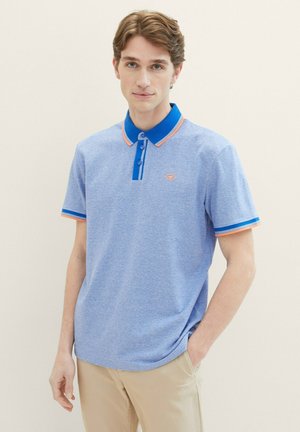 Helles blaues Poloshirt mit strukturiertem Finish, versehen mit einem blauen Kragen und orangefarbenen Akzenten an den Ärmeln, sowie einem kleinen Logo auf der Brust.