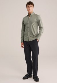 Hellgrünes Button-Up-Hemd mit Kragen, langen Ärmeln und taillierter Passform, kombiniert mit schwarzen Hosen und schwarzen Schuhen.