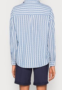 Camicia a maniche lunghe di colore azzurro chiaro con strisce verticali bianche e piccoli motivi a pois blu, abbinata a pantaloni corti navy. Tessuto morbido con dettagli in bottoni.