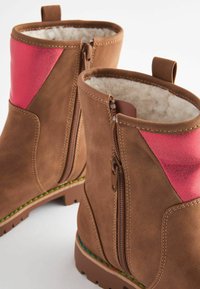 Botas de tobillo marrones con acentos rosas, cierre de cremallera lateral, forro suave y superficie texturizada. Cuenta con una suela robusta con borde colorido.