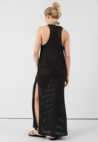 Robe maxi noire sans manches avec un design en tricot en maille. Caractéristiques fentes latérales hautes et coupe fluide, accentuant la respirabilité et le mouvement.