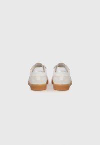 White suede sneakers with a tan rubber sole, featuring a logo on the heel and a simple, minimalist design.