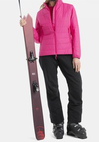 Růžová zateplená bunda s quiltovaným designem; černé lyžařské kalhoty; kaštanové lyže s černými vázáními; černé lyžařské boty se stříbrnými akcenty.