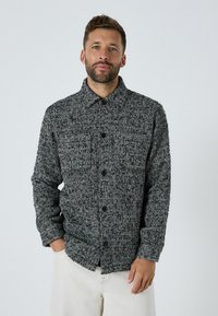 Košeľa s herringbone vzorom v čierno-bielej farbe, vyrobená z textúrovanej látky, so golierom a prednými vreckami.