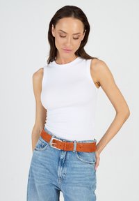 Vitt ribbat ärmlöst linne kombinerat med högmidjade ljusblå denimjeans och ett orange kordflöjelbälte med en silverfärgad spänne.