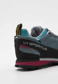 Pelēki zamšādas un sieta pārgājienu apavi ar zilu akcentu, melnu papēdi, rozā vidusdaļu un aizmugures vilkšanas cilpu.