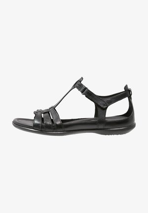 Sandalo in pelle nera con cinturini incrociati, chiusura alla caviglia regolabile, soletta piatta e dettagli testurizzati per una migliore presa.