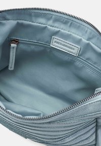 Interno della borsa in pelle blu texturizzata con un tessuto liscio e foderato, dotato di una tasca con zip e di un'etichetta del marchio cucita all'interno.