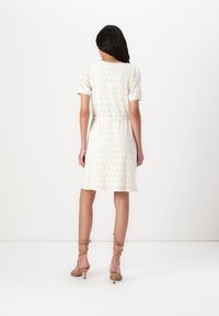 Rochie crem cu mâneci scurte, având un model geometric din dantelă și un talie ajustată. Asortată cu sandale cu toc bej.