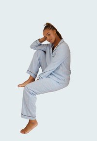 Ensemble de pyjama bleu clair avec un motif rayé et des accents en étoile rose. Comprend des passepoils noirs contrastants et une coupe décontractée. Tissu doux et lisse.