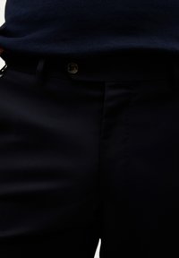Pantalones oscuros de navy hechos a medida, elaborados en una tela suave, con un diseño de frente plano, presillas para cinturón y cierre de botón.