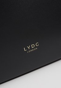 Surface en cuir noir texturé avec texte embossé doré indiquant LYDC LONDON près du coin inférieur droit.