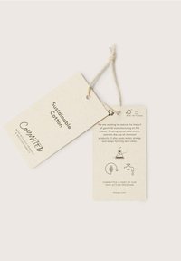 Hållbara bomullsskyltar i beige återvunnet papper, med svart text och miljövänliga ikoner för att visa plaggets påverkan.