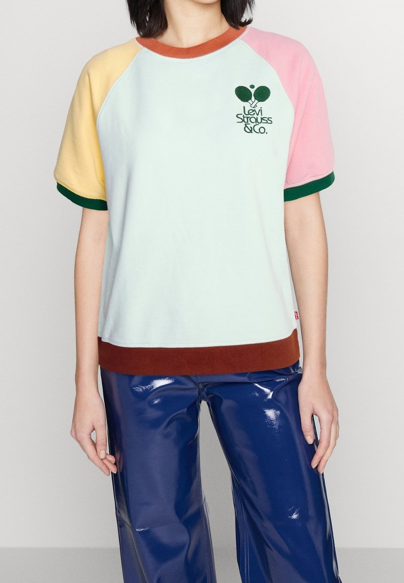 T-paita raglan-hihalla pastelliväreissä: mintunvihreä vartalo, keltaiset, vaaleanpunaiset ja vihreät hihat, ruskea helma, jossa on "Levi Strauss & Co." -logo.
