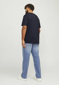 Marineblå bomuldst-shirt med korte ærmer, parret med lyseblå lige bukser og hvide sneakers. Simpelt, afslappet design.