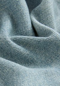 Stof de denim de culoare albastru deschis, prezentând o țesătură fină în diagonala, cu textură vizibilă și variații subtile de culoare, creând un aspect moale și neted.