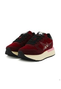 Sneaker in suede rosso con lacci neri, colletto imbottito e suola crema a contrasto. Presenta un logo riflettente e dettagli testurizzati.